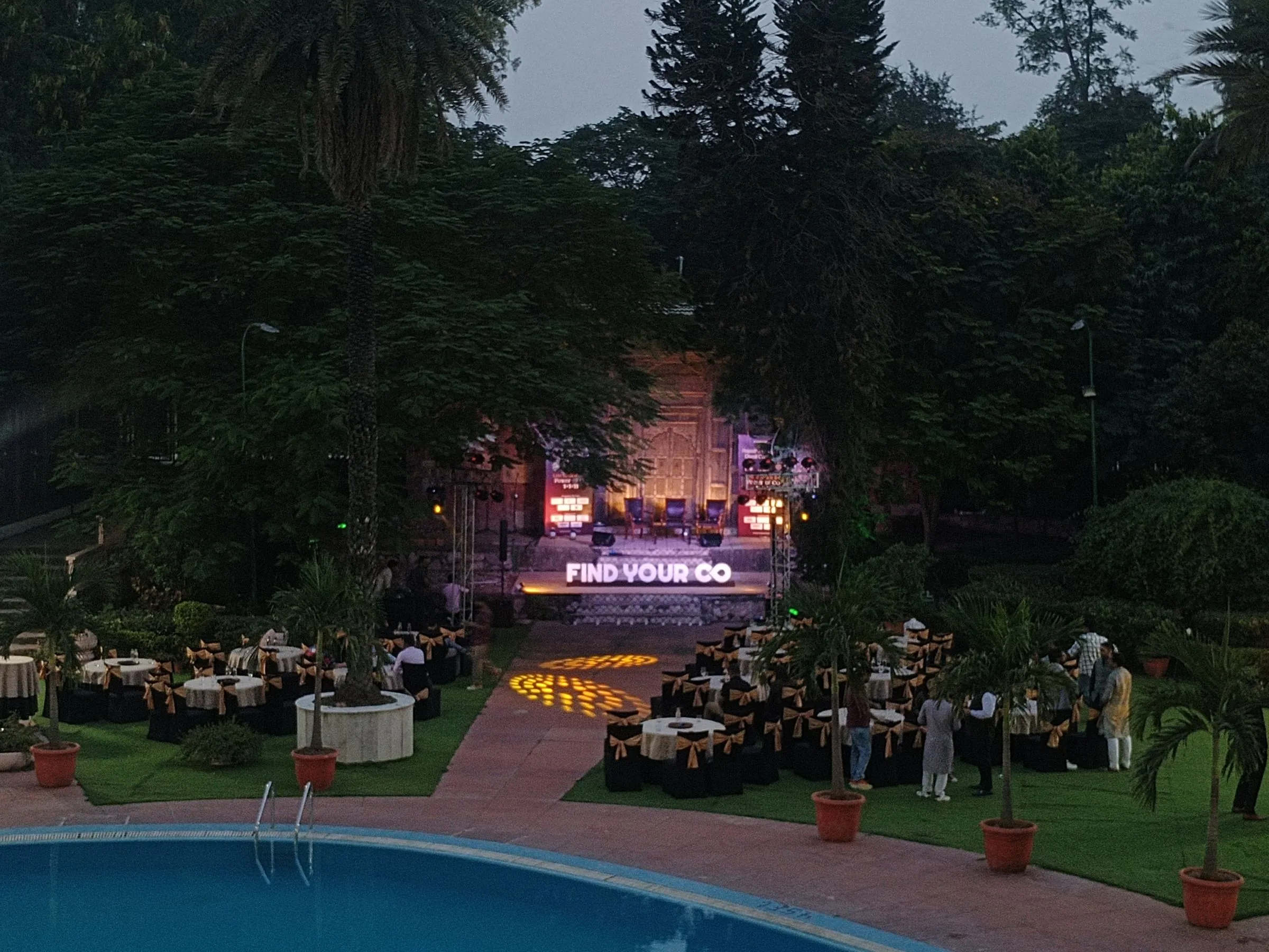 Aerial view of last year's open-air Copreneurs evening at dusk, with tables set on the lawn and the stage lit
