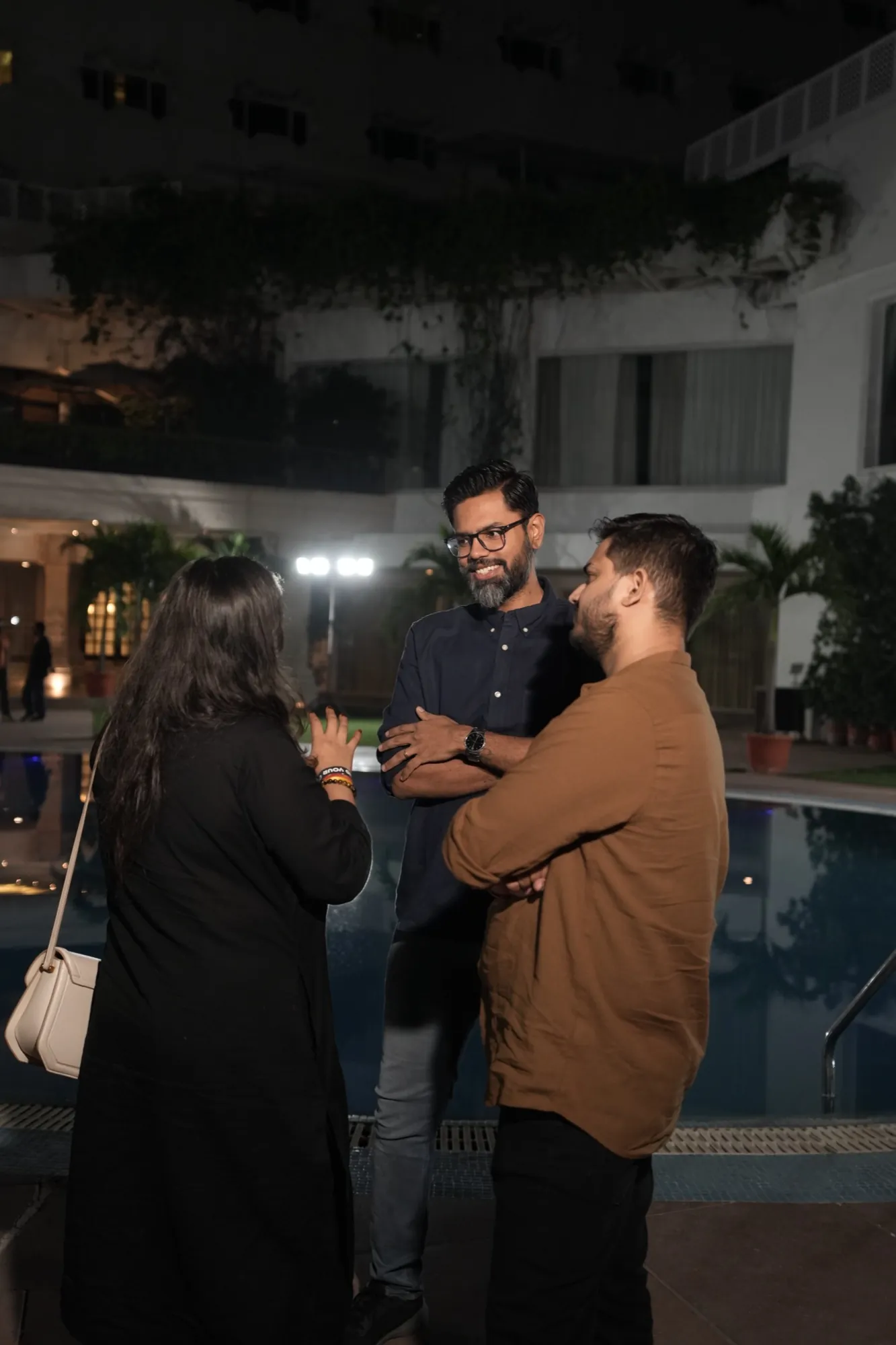 Three people in close conversation by the pool at night